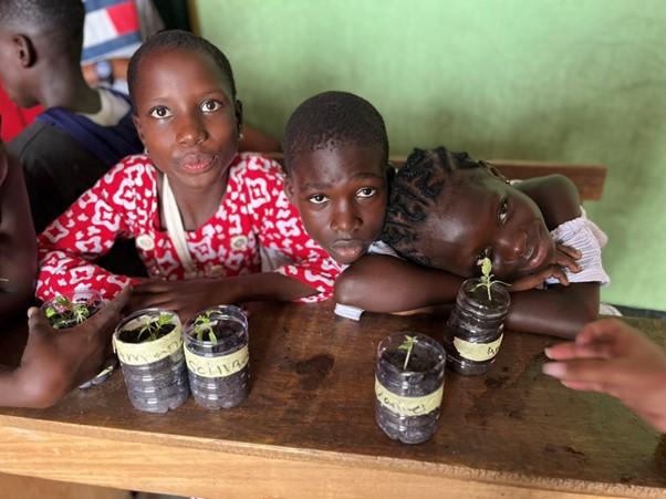 Trois collégiens assis à une table dans une salle de classe. 4 bouteilles sur la table contenant chacune une petite plante