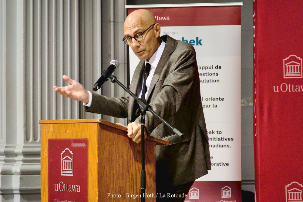 a man stands at a podium, it appears that he is speaking because his mouth is open and his hand is elevated