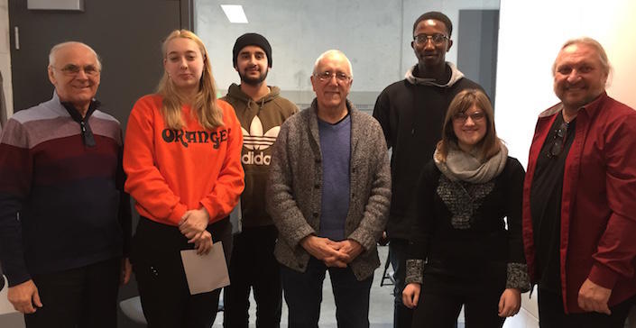 Cinq hommes et deux femmes, souriants, se tiennent debout dans une salle de classe.