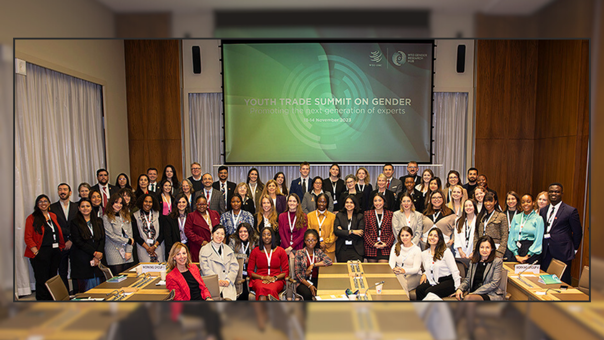 Un grand groupe de personnes sont assises et debout, face à la caméra, dans une grande salle de réunion. Derrière elles, un écran affiche les mots "Youth Trade Summit on Gender" (Sommet des jeunes sur le commerce et l'égalité des genres)