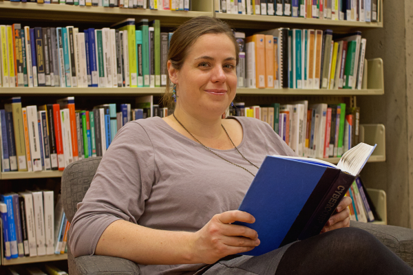 Myriam Legault-Beauregard assise sur un fauteuil devant une bibliothèque tenant un livre
