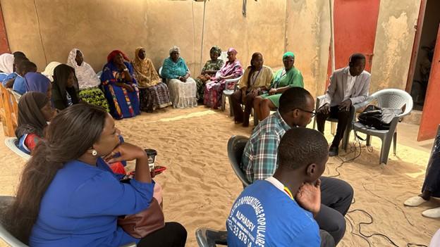 A group of African people sitting in a circle on white chairs