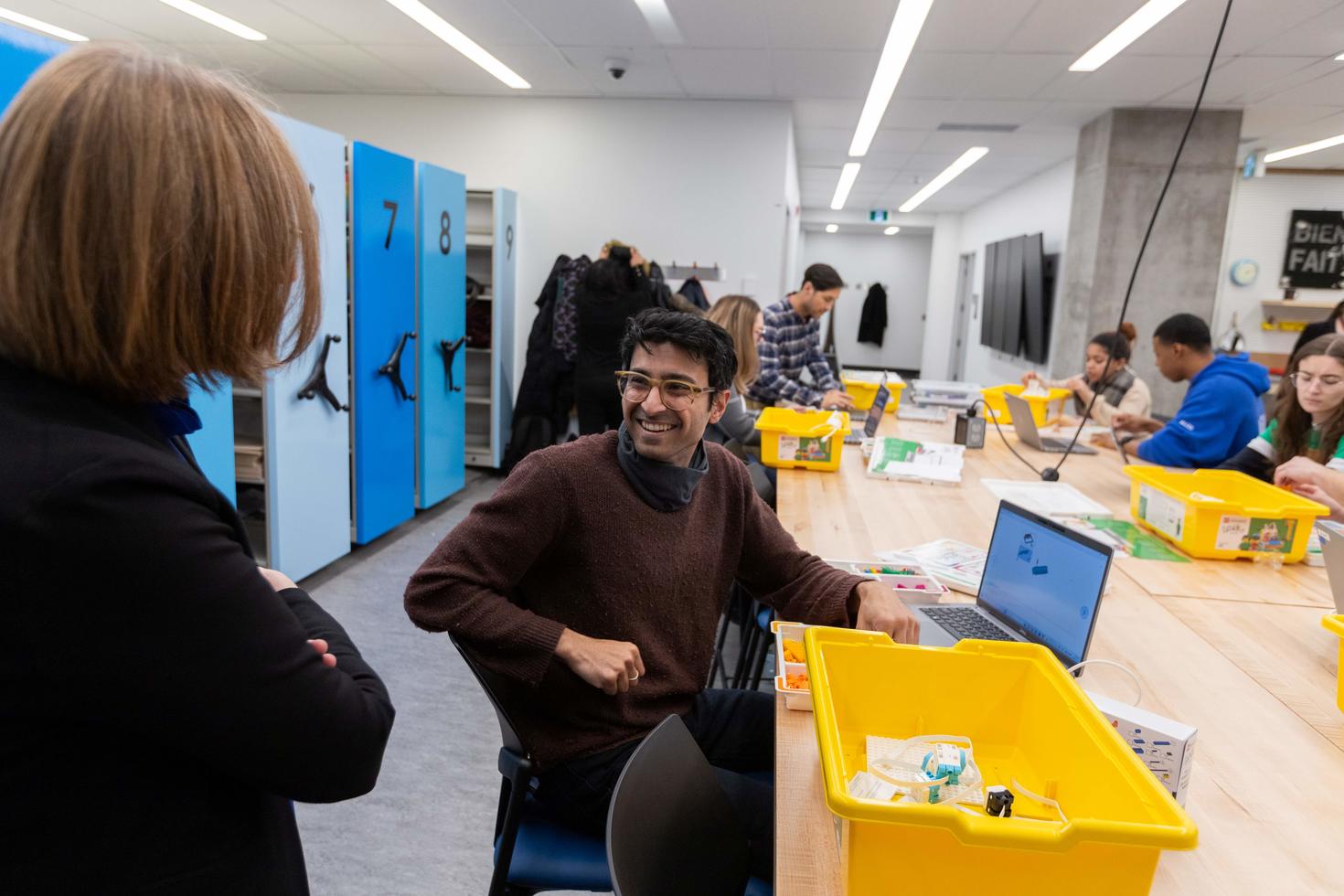 Étudiant dans un laboratoire maker souriant à un membre du corps professoral.