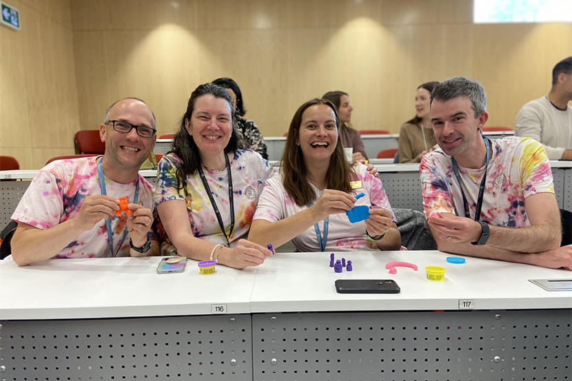 Smiling eachers wearing tie-dye shirts, holding play dough. 