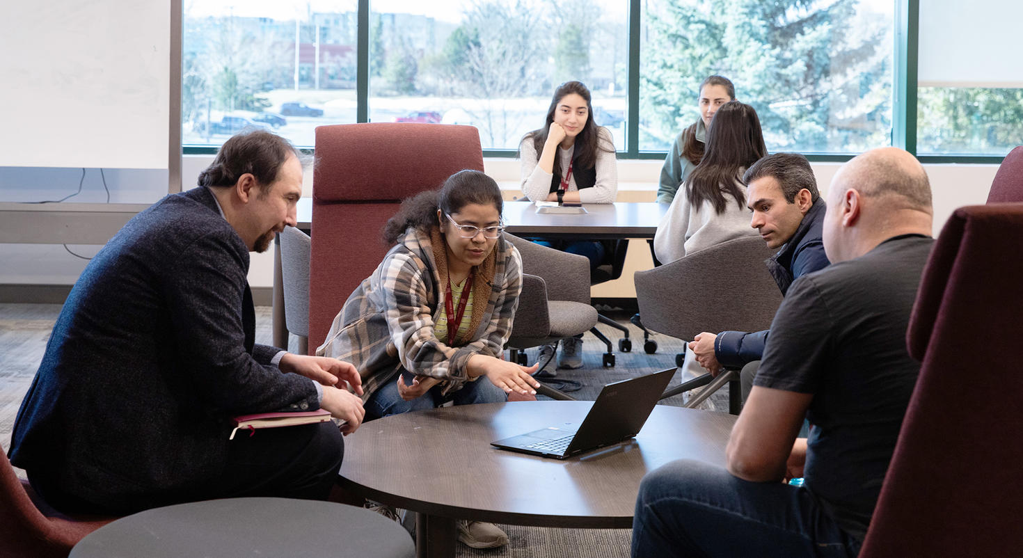 A group of professor looking at a student pointing at her computer