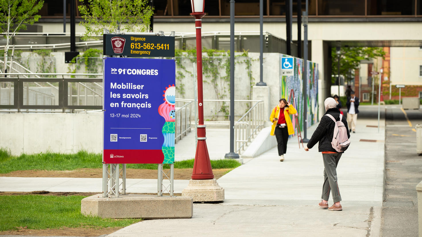 Personnes passant devant le panneau ACFAS sur le campus