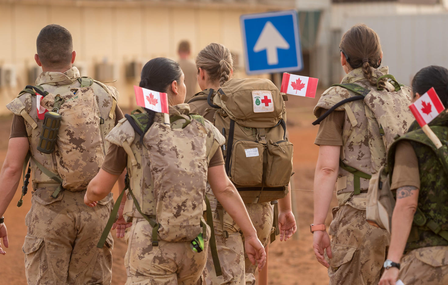 Des militaires en tenue de camouflage s'éloignent, chacun portant un sac à dos sur lequel est accroché un drapeau canadien.