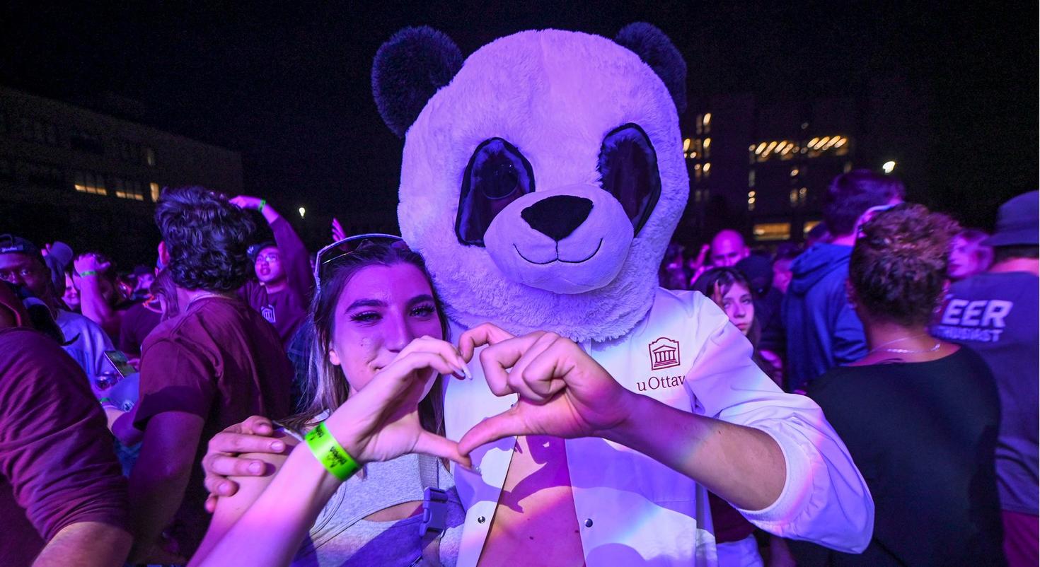 Une étudiante et un autre étudiant portant un masque de panda joignent leurs mains pour former un cœur. 