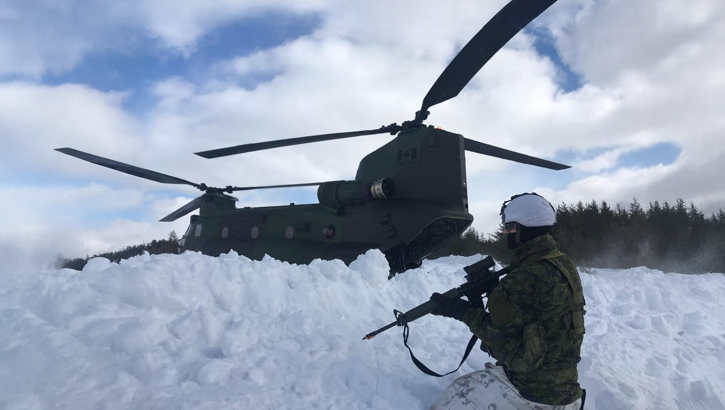 Un soldat agenouillé dans la neige à côté d'un hélicoptère