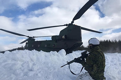 A soldier kneeling in the snow beside a helicopter