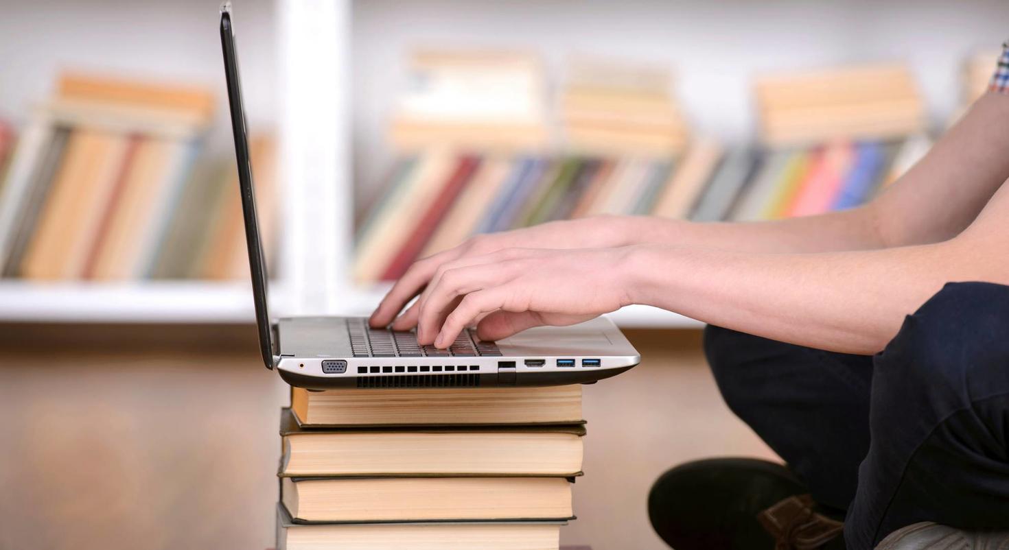 laptop on pile of books with student typing 