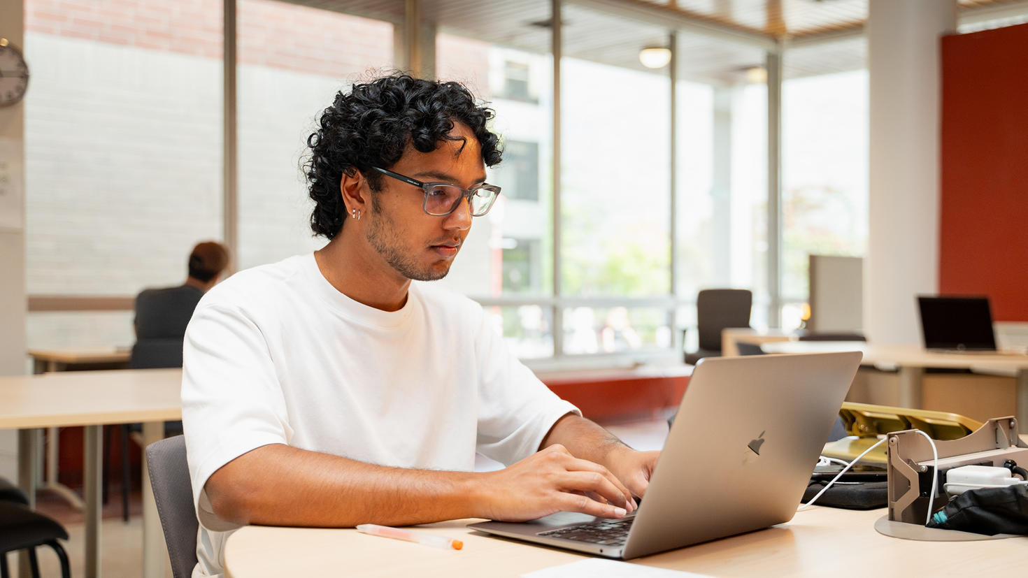 Un étudiant est assis à une table et étudie avec un ordinateur portable.