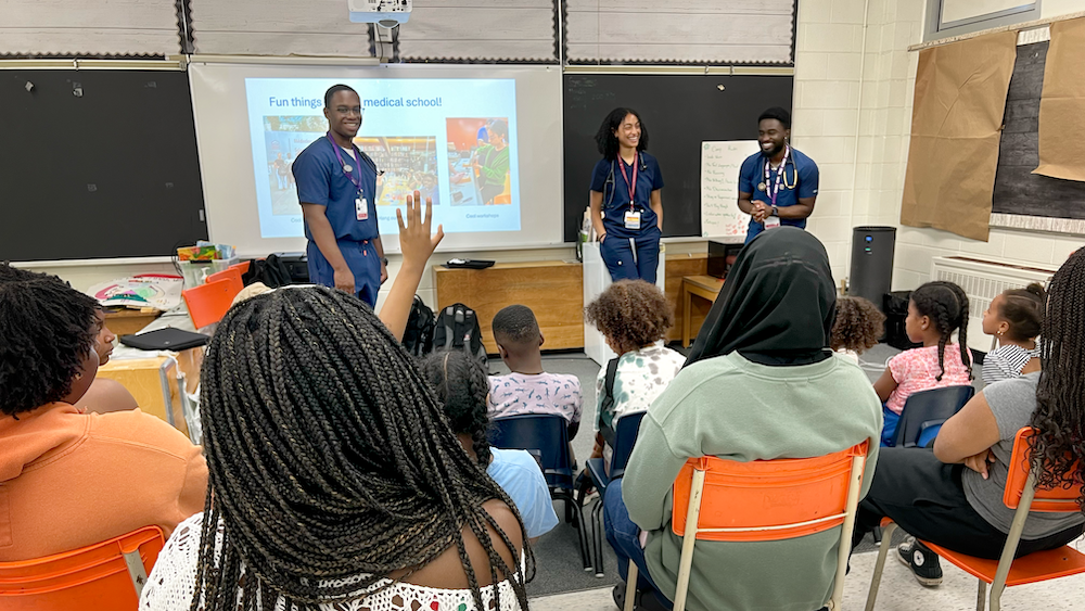 Trois étudiants font une présentation à des jeunes dans une salle de classe.