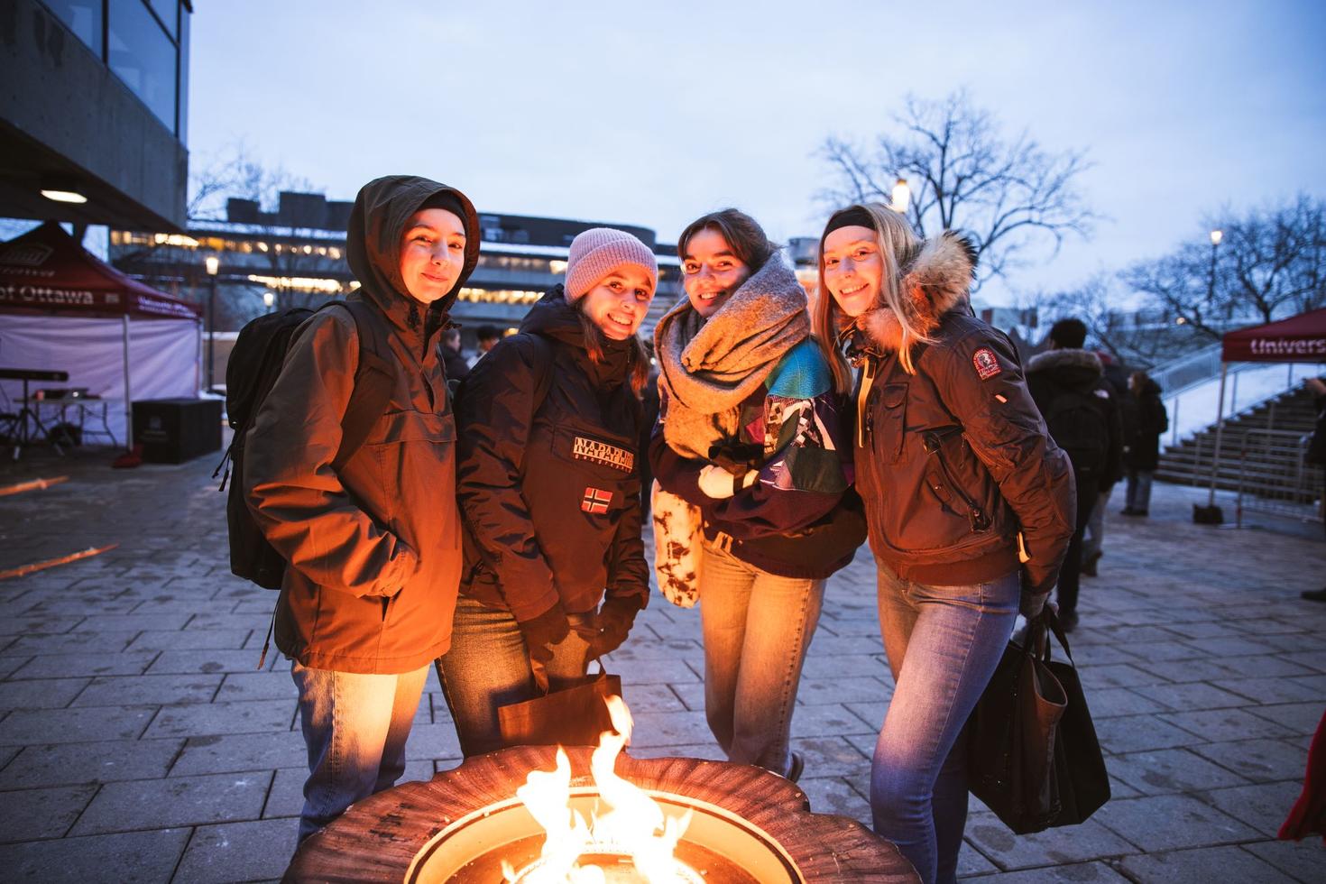 Quatre étudiantes se réchauffent autour d'un feu en plein air pendant l'hiver.