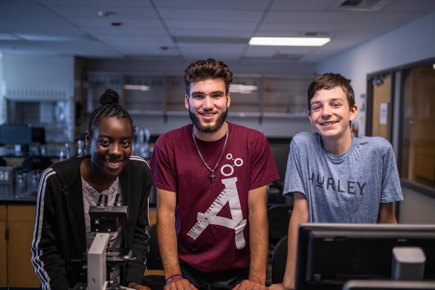 Trois youth smiling in a lab. 
