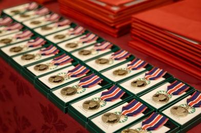 Plusieurs Médailles du couronnement du roi Charles III sur un présentoir. La médaille est circulaire, de couleur argent et attachée à un ruban bleu foncé, rouge vif et blanc.