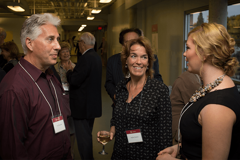 Trois personnes et d'autres en arrière-plan qui discutent lors d'un événement.