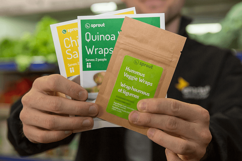 Gros plan des mains d’un homme tenant deux fiches de recettes et un sachet d’assaisonnements.