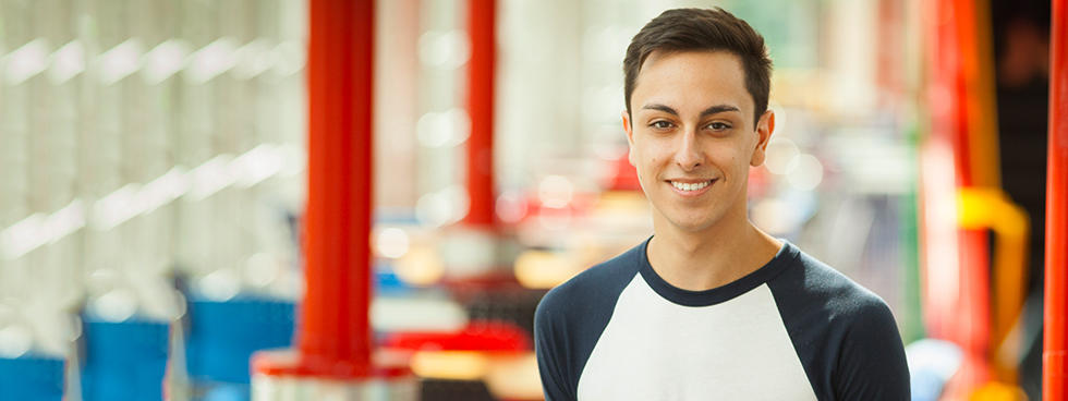 Un jeune étudiant souriant à la caméra. | A male student walking towards the camera, smiling.