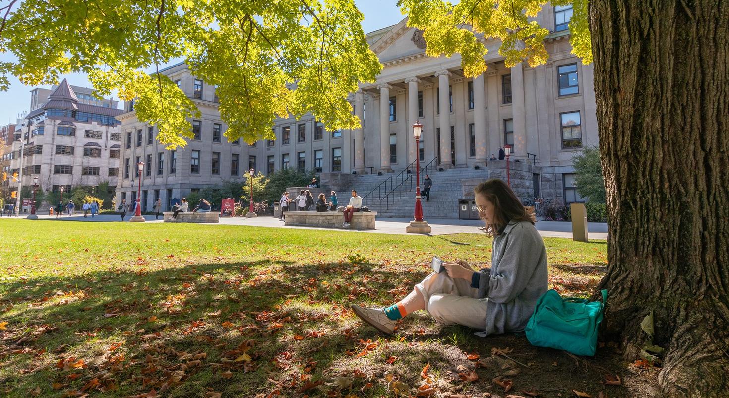 A student studying under a tree on the lawn in front of Tabaret Hall.