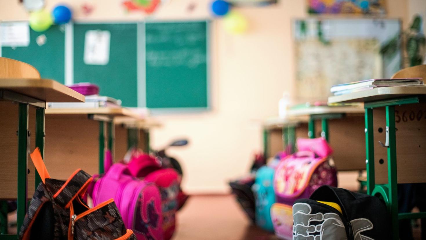 Salle de classe avec des sacs à dos près de chaque pupitre.
