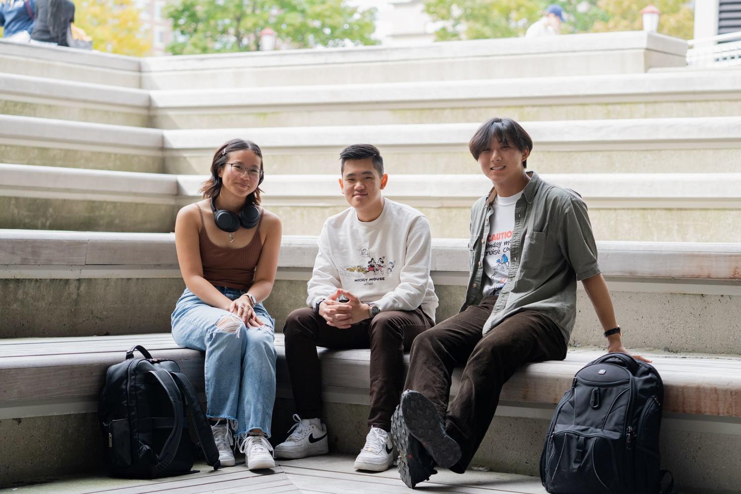 Three students sitting on concrete steps in the sunshine on the University of Ottawa campus.