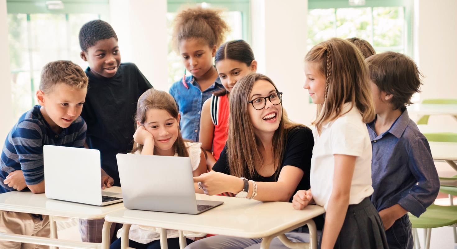 Une ado montrant à un groupe d'enfants comment utiliser un ordinateur portable.