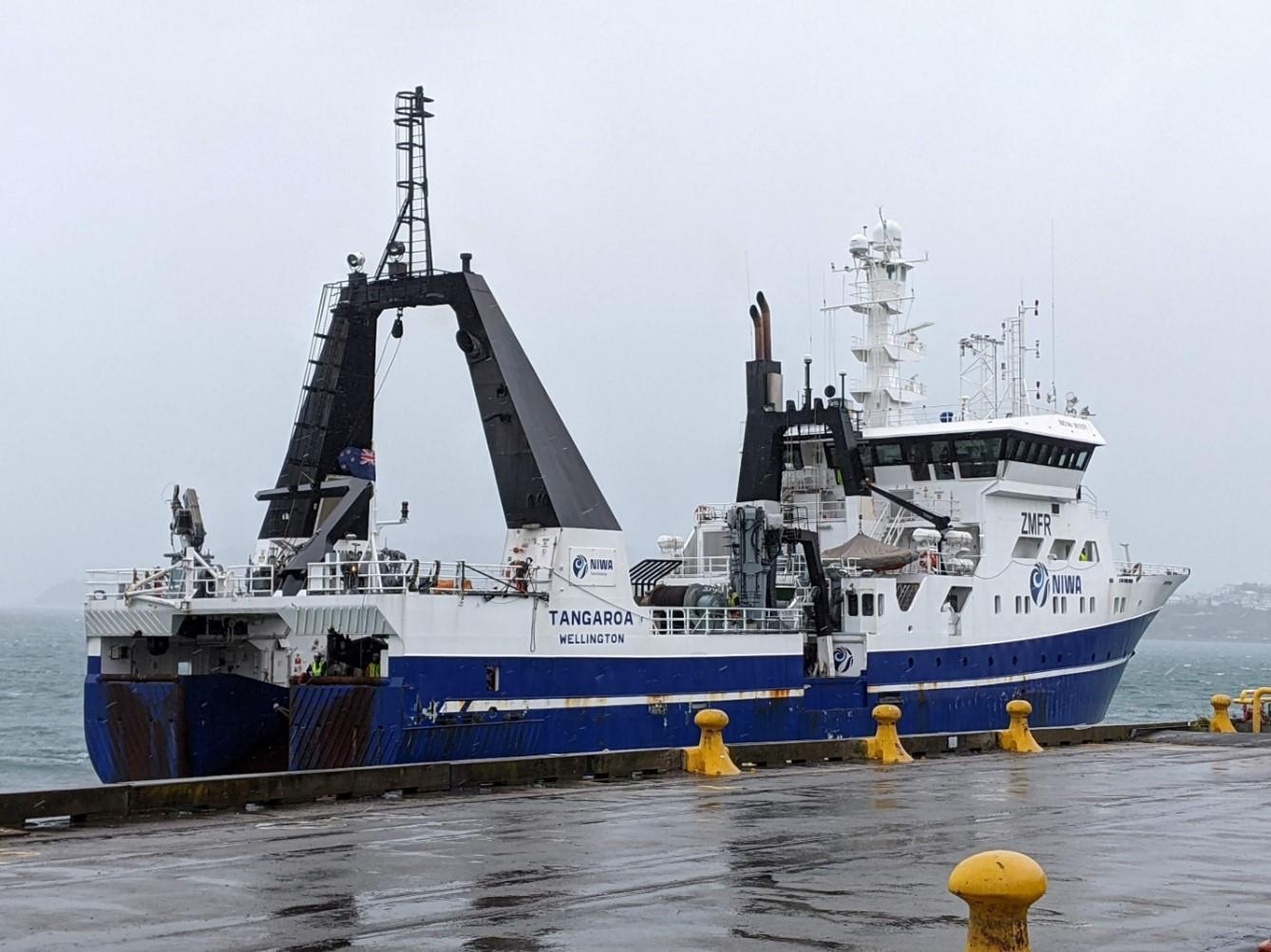 The research vessel Tangaroa, adorned with the flag of New Zealand, is docked at the Wellington pier. This vessel is central to the ELVES project, which studies seismic activity in the Hikurangi subduction zone off the coast of New Zealand.