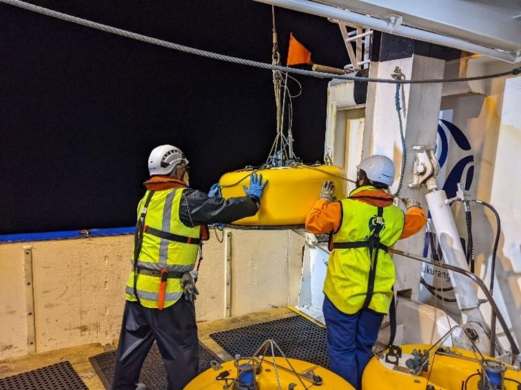 Deux ouvriers préparent soigneusement un sismomètre de fond de mer en vue de son déploiement sous les vagues.