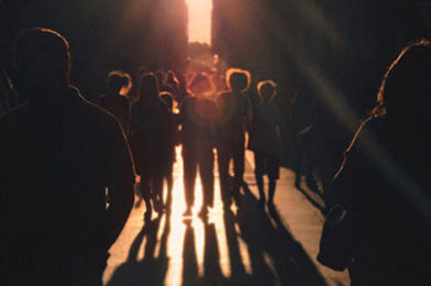 Une foule en silhouette avance sur une rue baignée de soleil, projetant de longues ombres.
