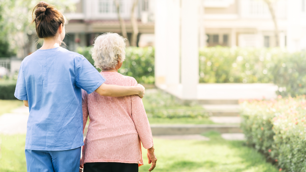 Une professionnelle de la santé accompagne un patient âgé dans un jardin.