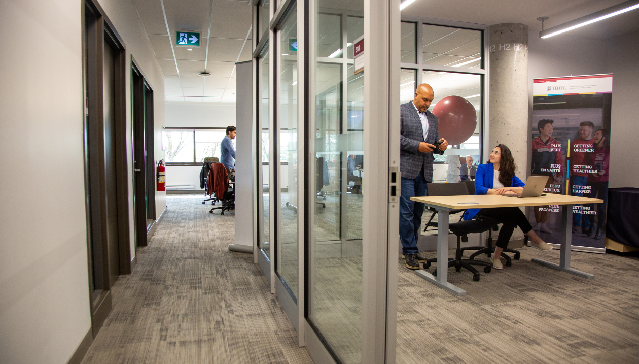 Modern office space with glass-walled rooms, a man on his phone, and a woman working at a desk.