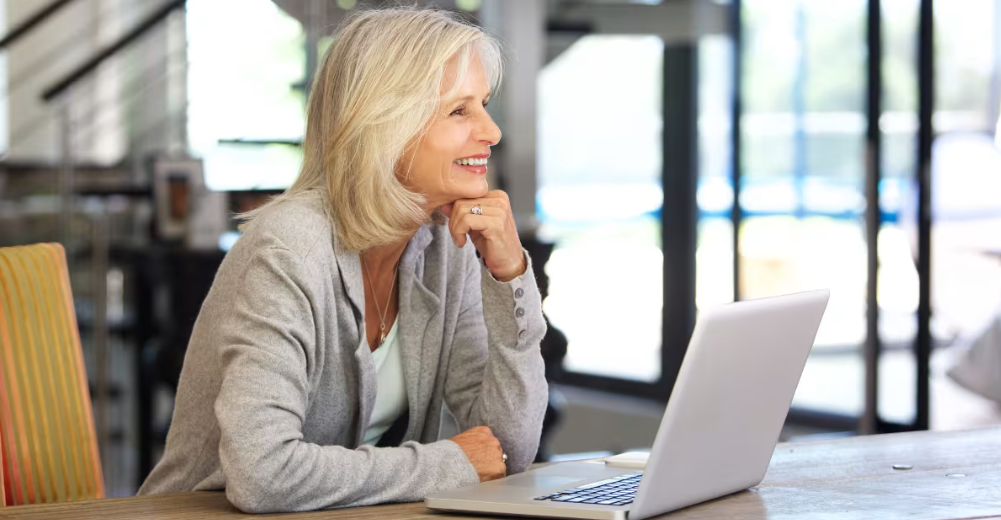 Smiling woman sitting at a table looking at a laptop screen.