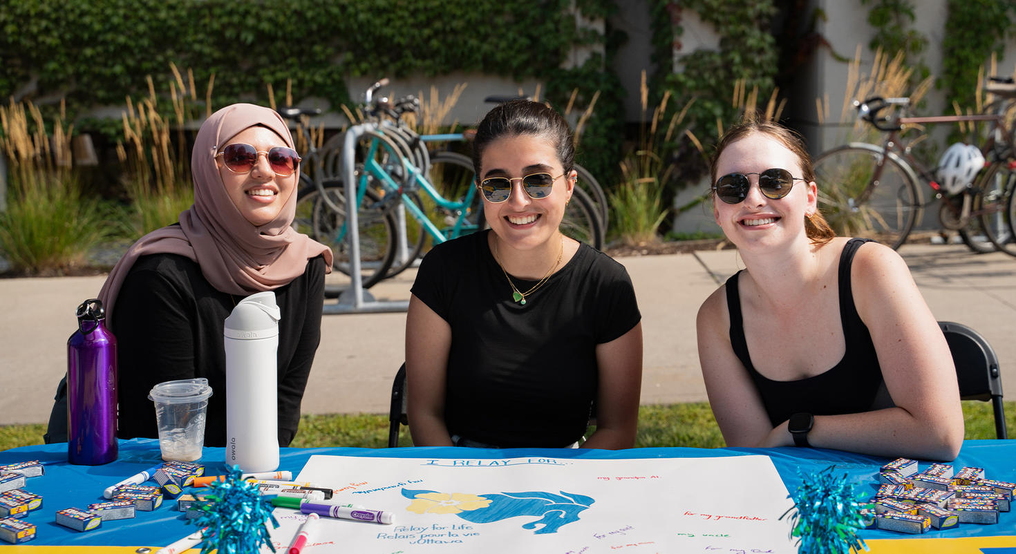 Three students sit at a table at the Club Fair in 2024. 