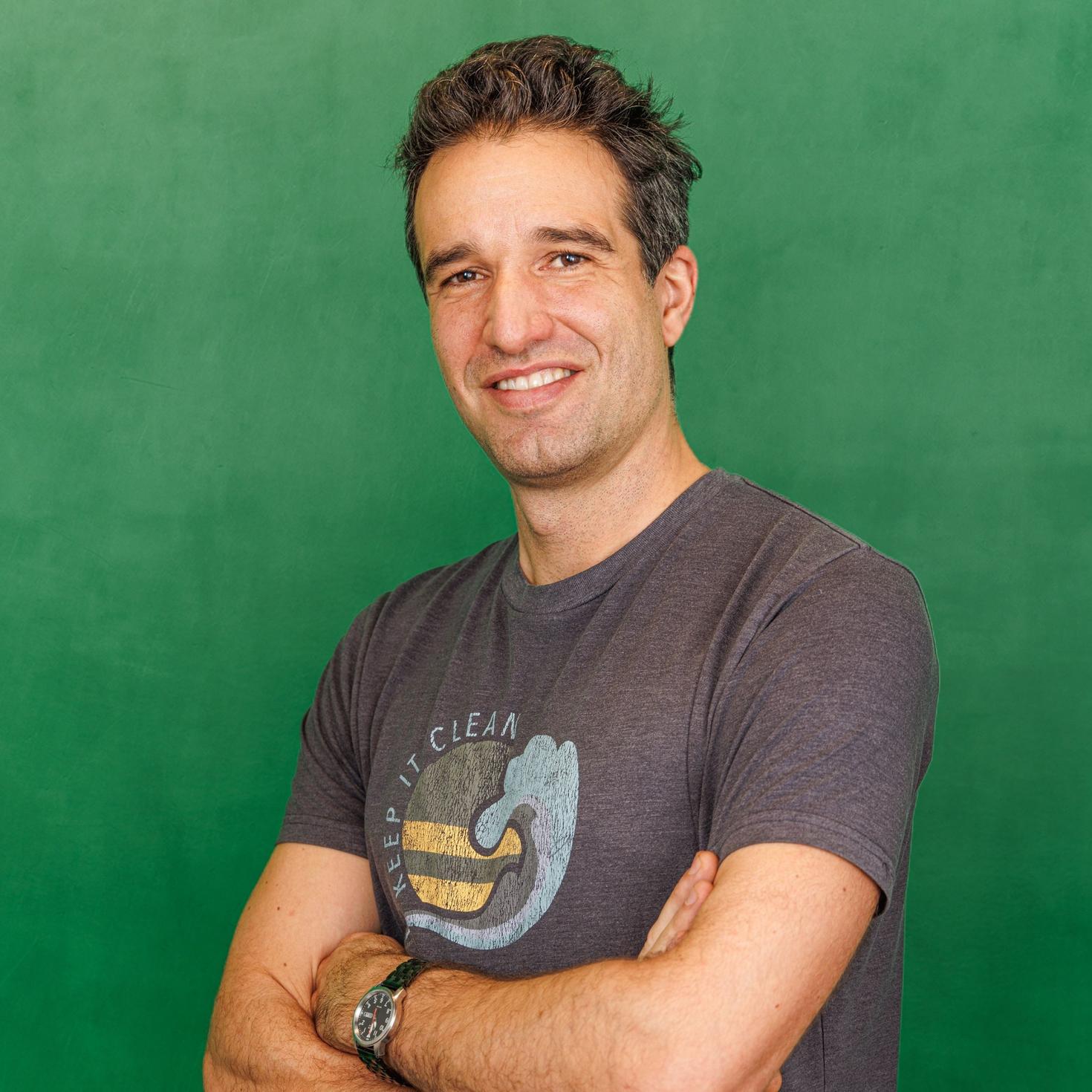 Olivier Rousseau, a PhD graduate in mathematics, stands, smiling with arms crossed, in front of a green background. He’s wearing a T-shirt that reads, “Keep it clean.”