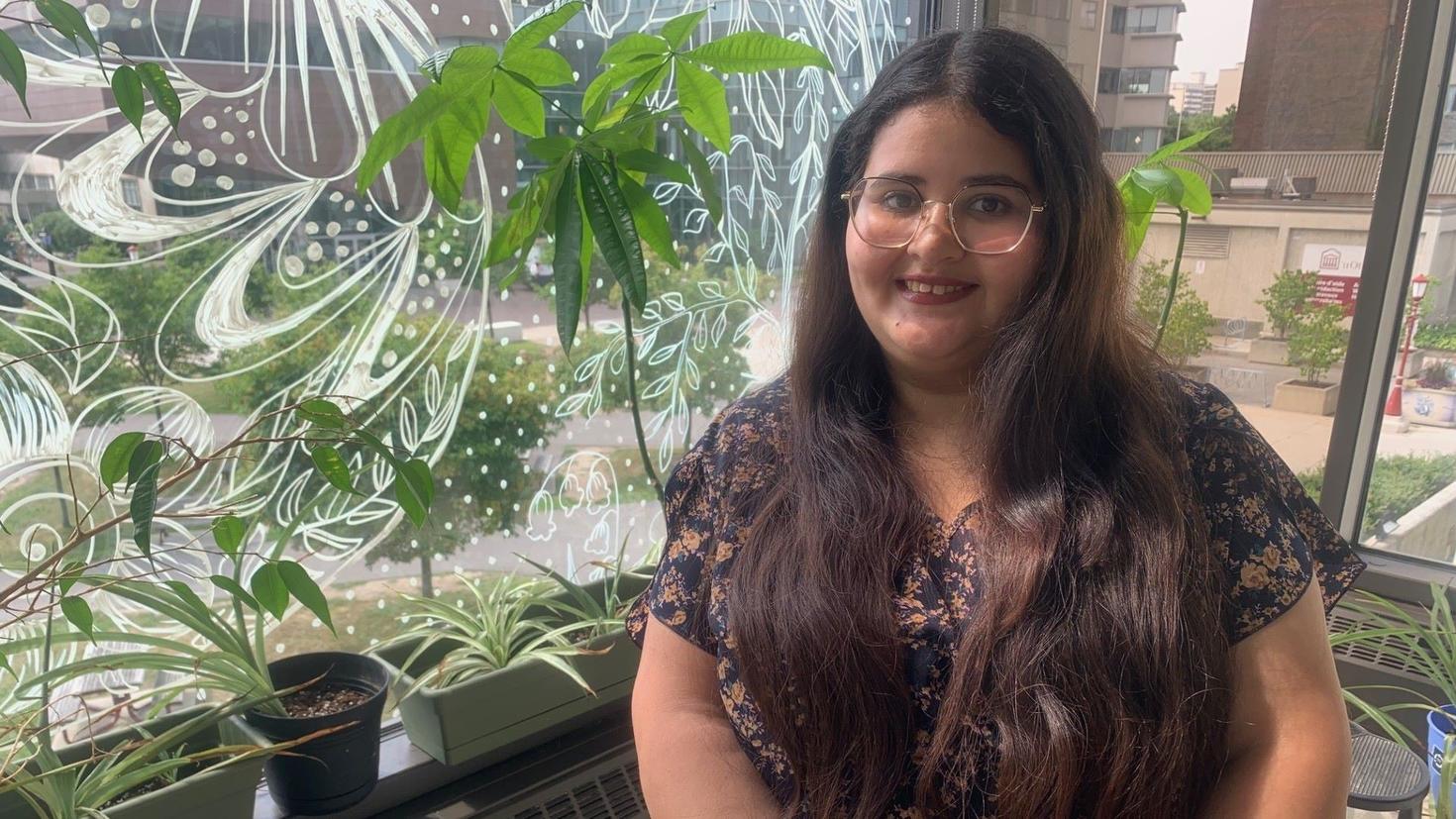 Keltoum Dassar sits next to a window surrounded by plants in the wellness plant room.
