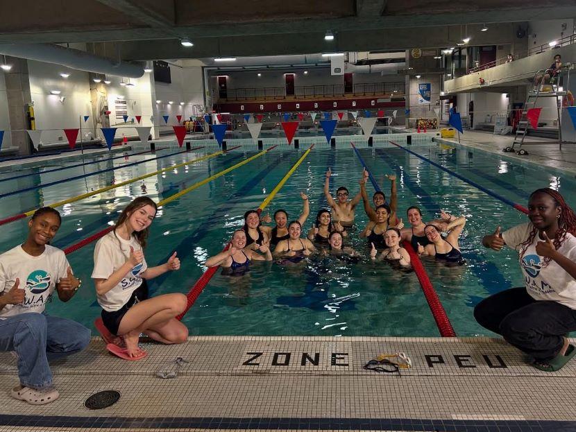A group of student volunteers in the SWAM club give a thumbs up and cheer in the uOttawa swimming pool.