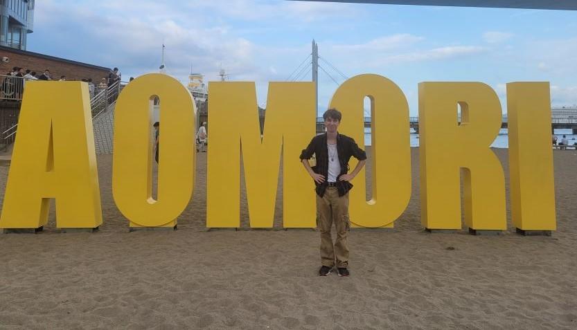 Blake devant le panneau indiquant la ville d'Aomori.