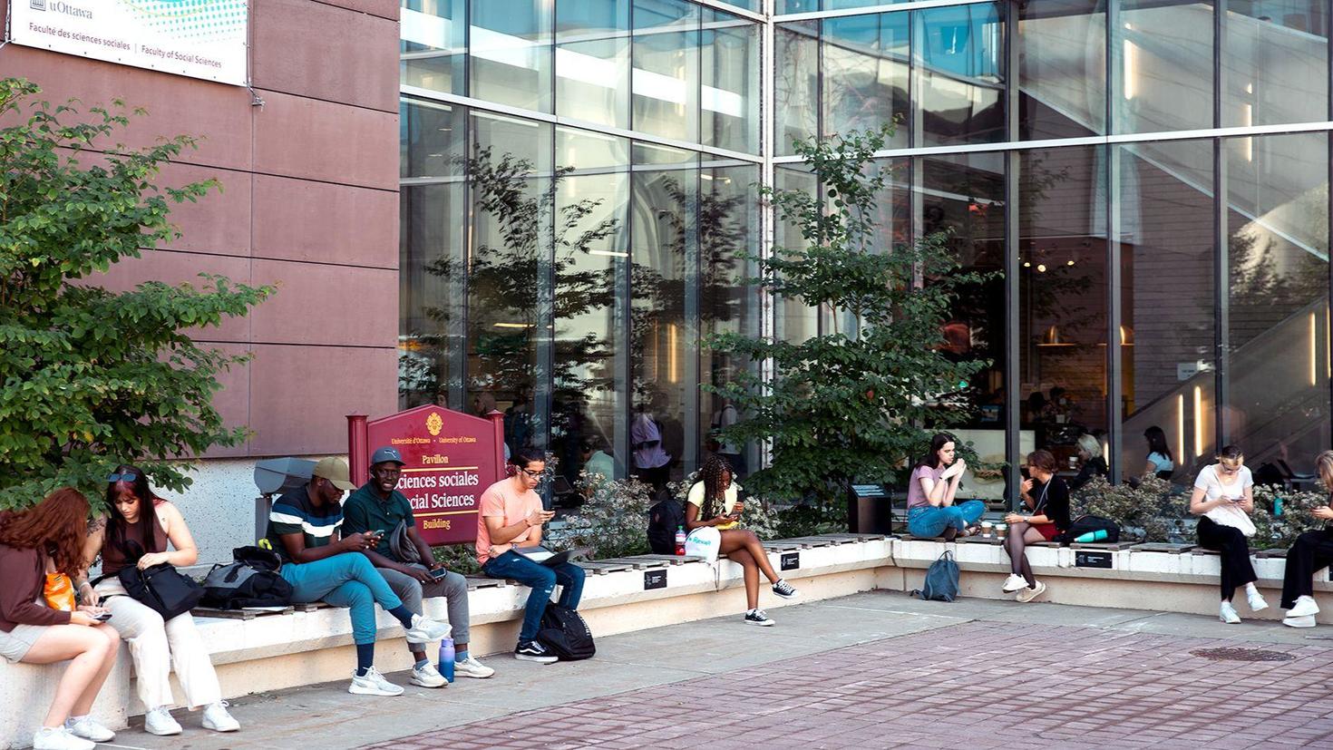 Students outside the Faculty of Social Sciences building near an Indigenous garden.