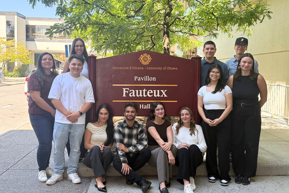 Students from the ILSG sit and stand in front of the Fauteux Hall sign