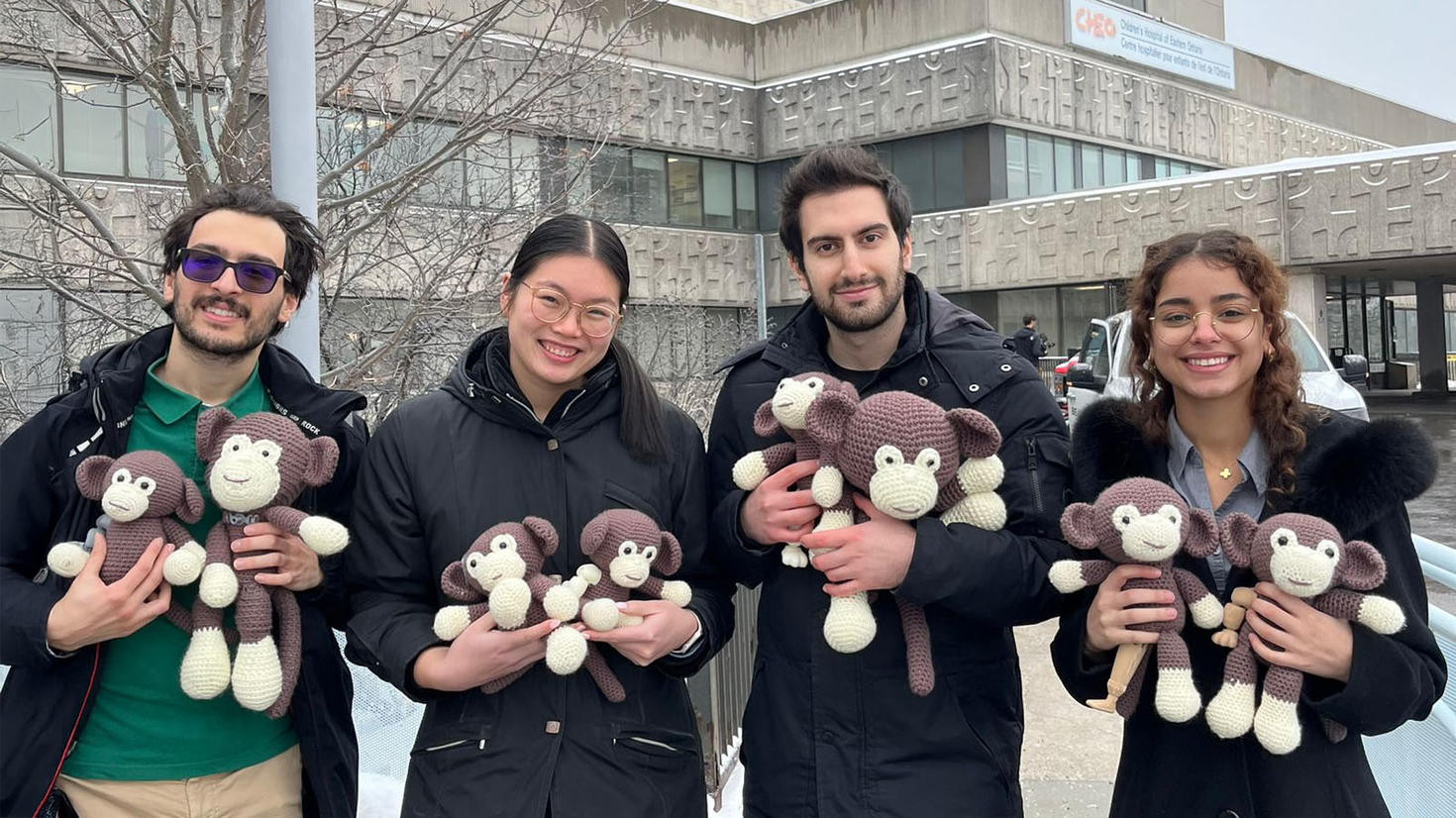 four medical students stand outside a children's hospital holding crocheted monkeys