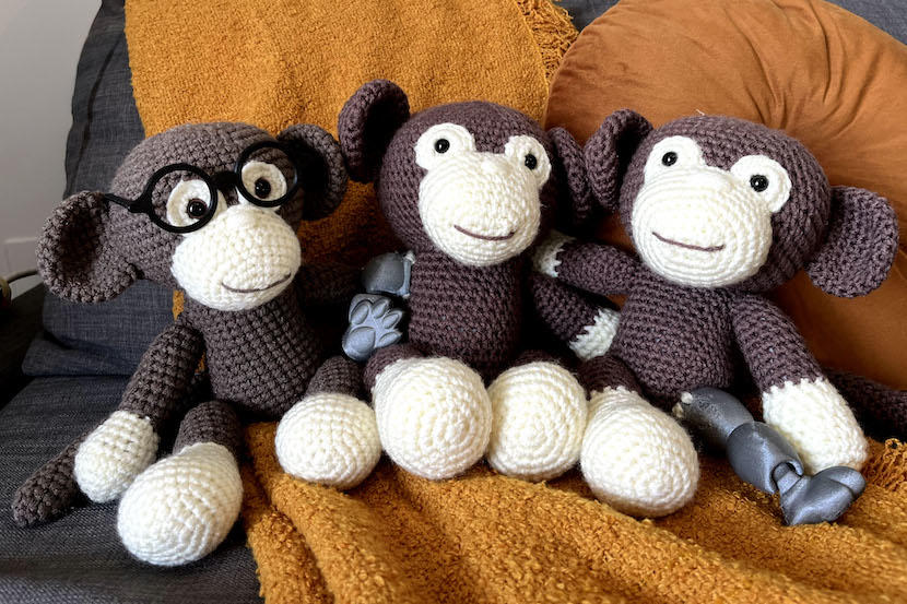 a crocheted monkey with glasses, one with a prosthetic arm, and one with a prosthetic leg.