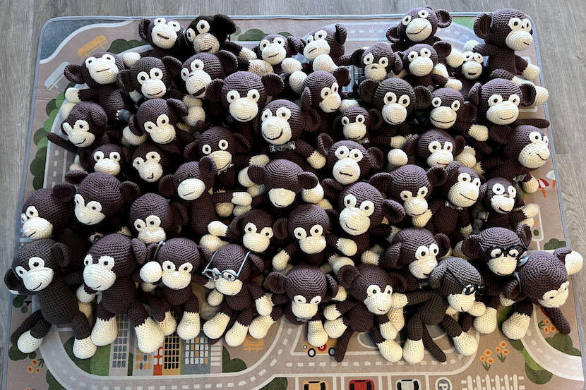 A large number of crocheted monkeys sitting on a carpet.