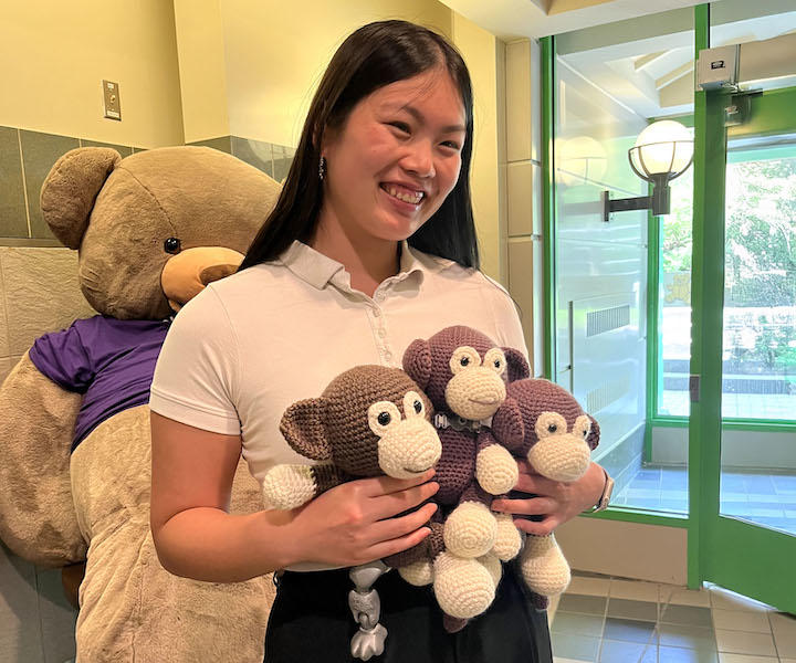 a medical student holding three crocheted monkeys.