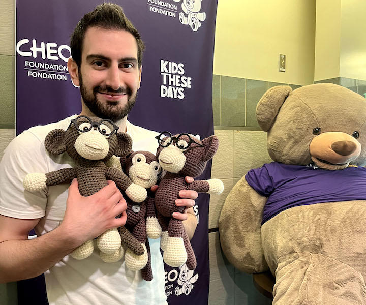 a medical student holding three crocheted monkeys.