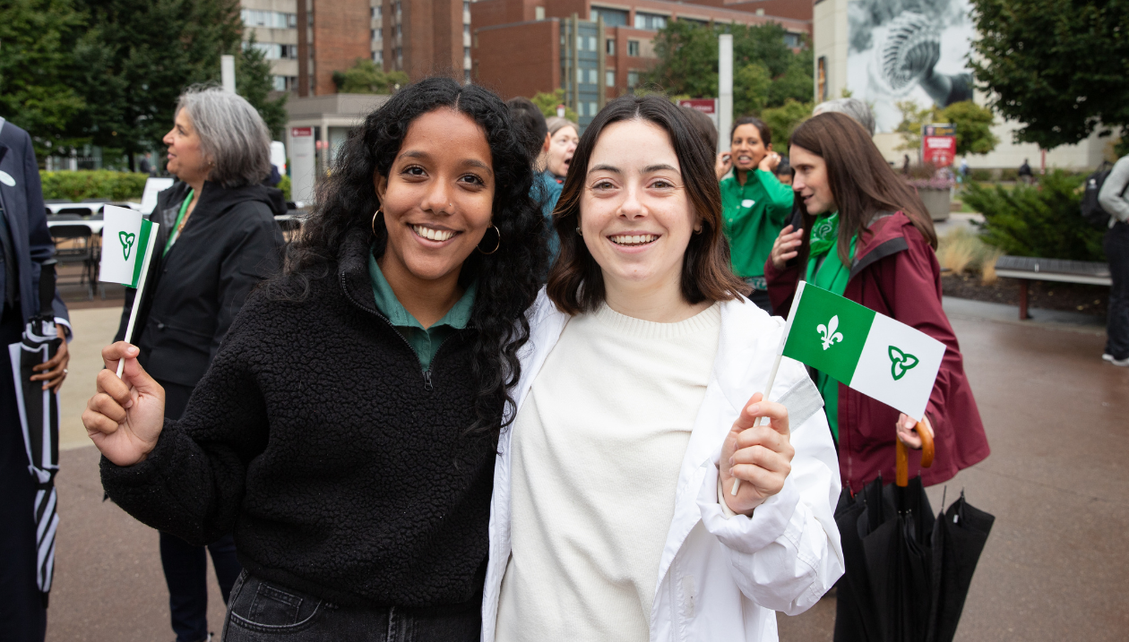 Deux étudiantes souriantes tiennent des drapeaux franco-ontariens lors du Jour des Franco-Ontariens et des Franco-Ontariennes à l’Université d’Ottawa.