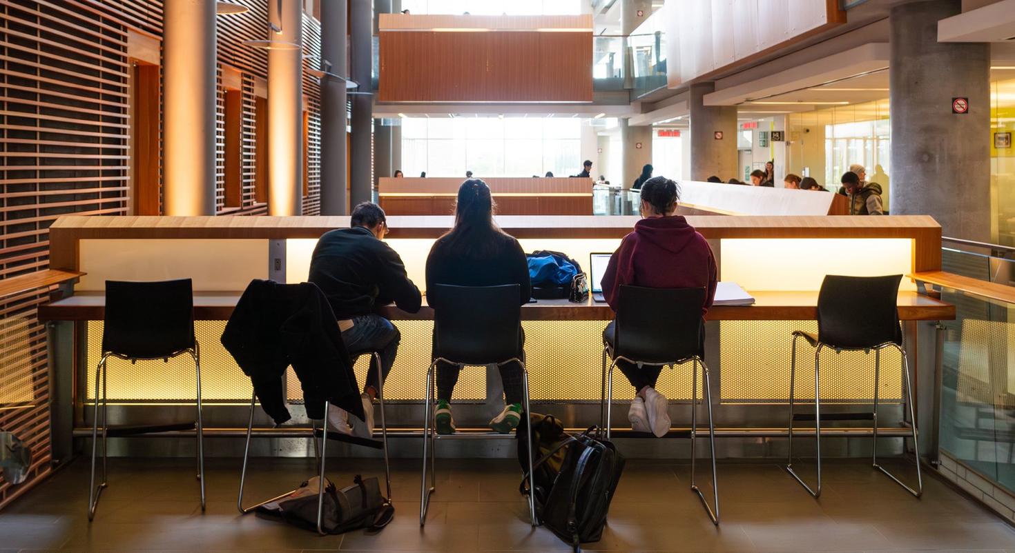 Three students in silhouette are studying inside the FSS Building.