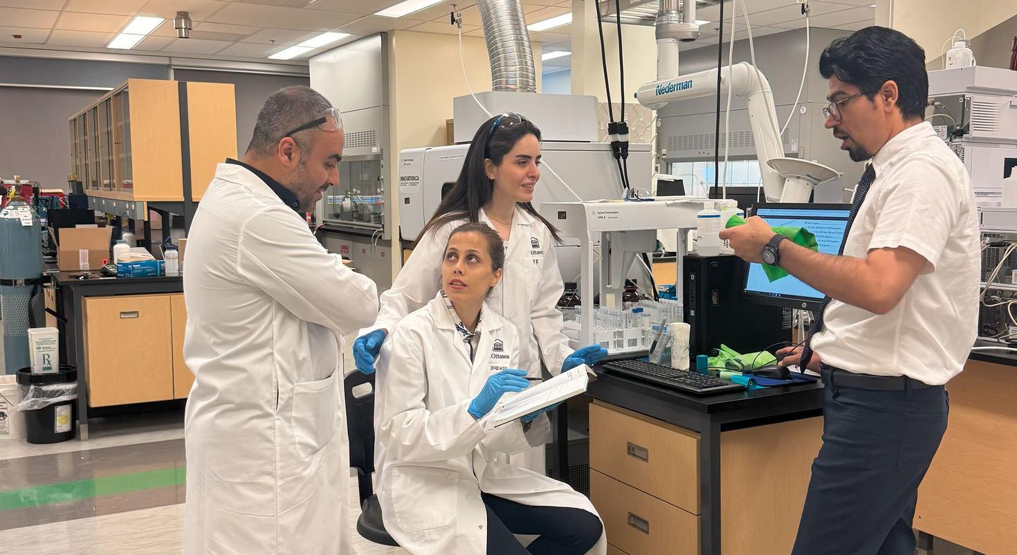 Four team members, three in lab coats, consulting in a lab.