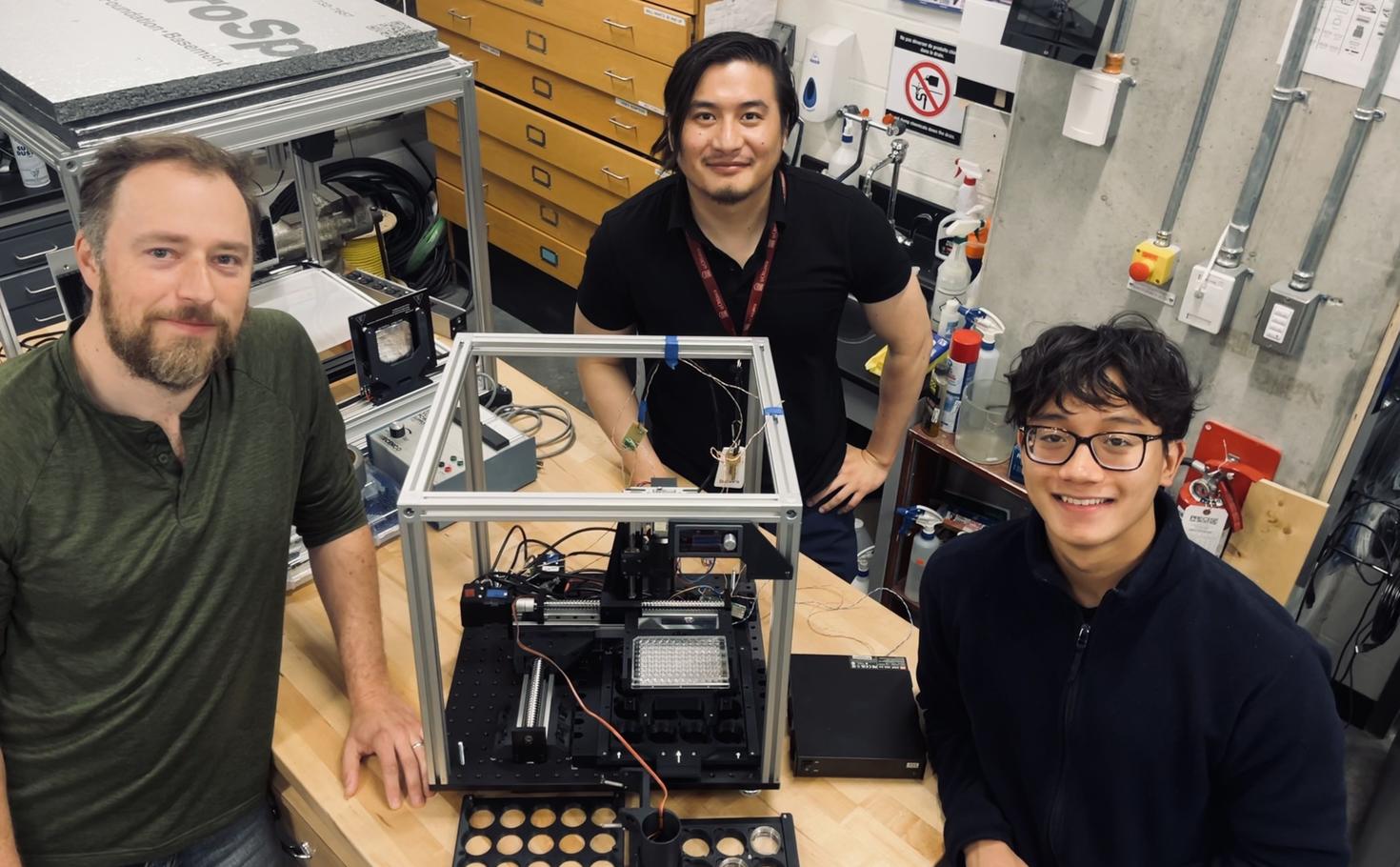 (Left to right) Lukasz Andrzejewski (senior technologist), Niepukolie Nipu (PhD student) and Huy Nguyen (undergraduate volunteer whom Niepukolie is currently mentoring). At the centre is the automated high-resolution and throughput system the team is developing to monitor the behaviour and cardiac activity of zebrafish embryos and larvae.