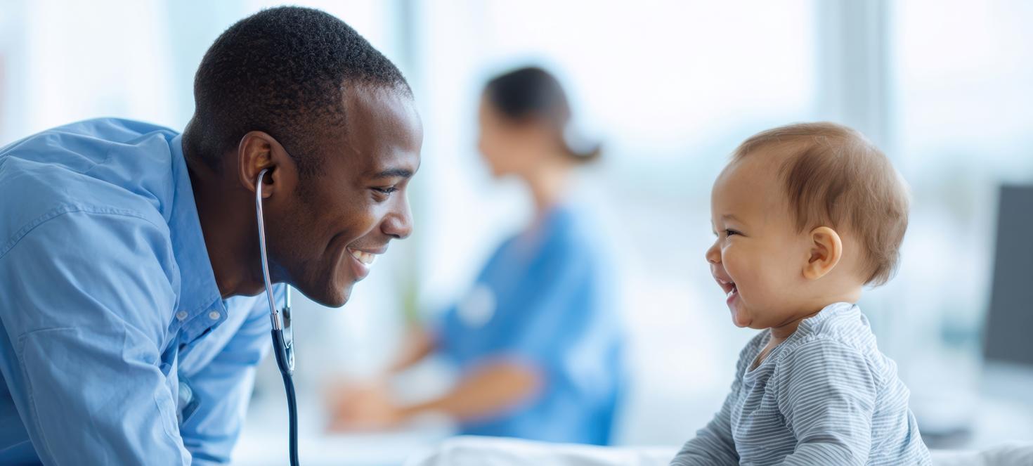 A doctor wearing a stethoscope smiles at a baby smiling back at him